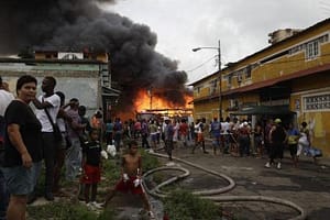 Residents of El Chorillo stand in the street as a fire burns in background.
